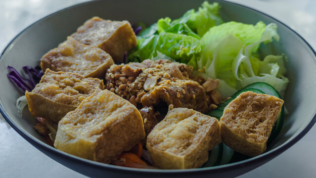 close up of fried tofu with roasted peanuts and fresh green salad in bowl, macro view showing crispy asian vegetarian meal featuring sliced cucumber
