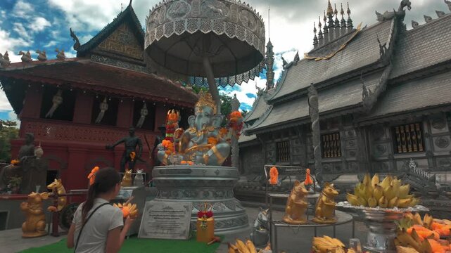 female tourist visiting Ganesha statue at Thai Silver Temple, woman pray hindu deity shrine with fruit offerings at Wat Sri Suphan, Chiang Mai Thailand 4k