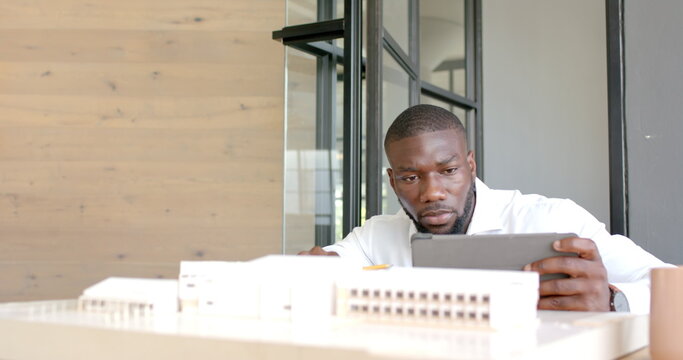 Architect working on building model and using tablet in modern office