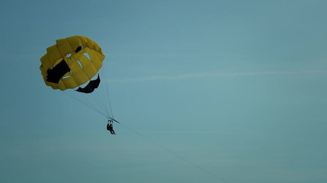 Two tourists parasailing under bright yellow smiley parachute behind motorboat over Adriatic Sea.