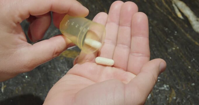Close up of hands tipping pills from a small medicine cup into an open palm above a dark countertop