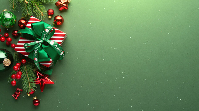 Green Christmas and Happy New Year holiday background with gift boxes, red ribbon bows and festive red ornaments, flat lay with copy space. Greeting card.