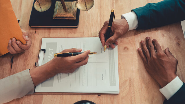 Client signing a legal contract agreement document during consultation with lawyer in office