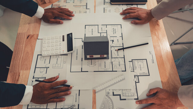 An architect and an engineer are discussing a house design project, with a scale model of the house placed on the table&mdash;a construction concept.