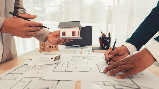 An architect and an engineer are discussing a house design project, with a scale model of the house placed on the table&mdash;a construction concept.