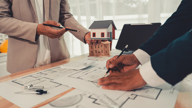An architect and an engineer are discussing a house design project, with a scale model of the house placed on the table&mdash;a construction concept.