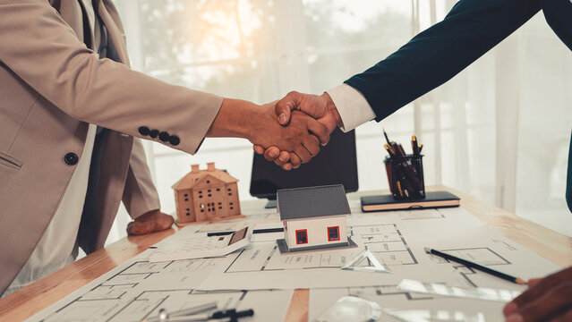 Architects and engineers shaking hands after successful meeting over house blueprint design project