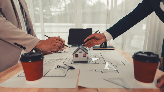 An architect and an engineer are discussing a house design project, with a scale model of the house placed on the table&mdash;a construction concept.