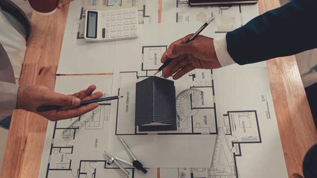An architect and an engineer are discussing a house design project, with a scale model of the house placed on the table&mdash;a construction concept.