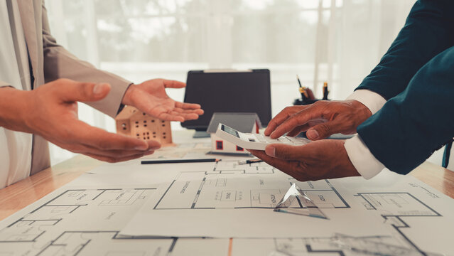 An architect and an engineer are discussing a house design project, with a scale model of the house placed on the table&mdash;a construction concept.