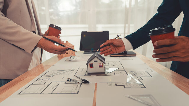 An architect and an engineer are discussing a house design project, with a scale model of the house placed on the table&mdash;a construction concept.