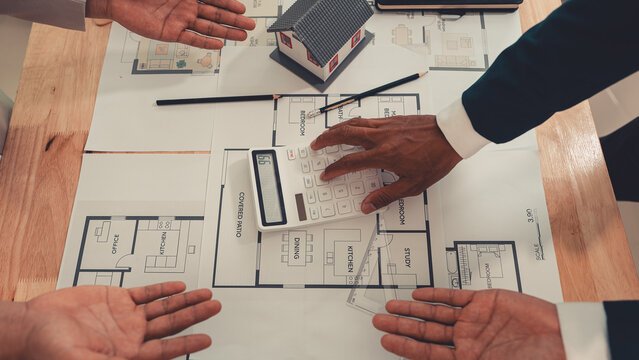 An architect and an engineer are discussing a house design project, with a scale model of the house placed on the table&mdash;a construction concept.