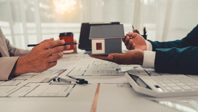 An architect and an engineer are discussing a house design project, with a scale model of the house placed on the table&mdash;a construction concept.