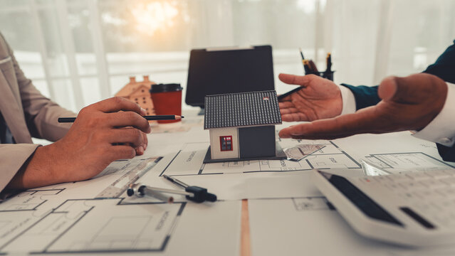 An architect and an engineer are discussing a house design project, with a scale model of the house placed on the table&mdash;a construction concept.