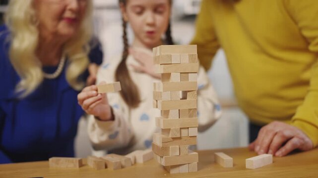 Little girl plays leaning tower game with granny and grandpa, family hobby