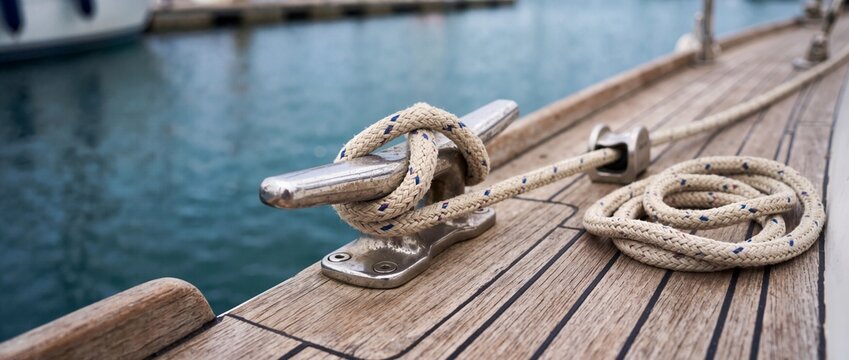 Mooring rope secured to a metal cleat on a yacht deck. Marine rope tied on teak wood boat deck at marina harbor