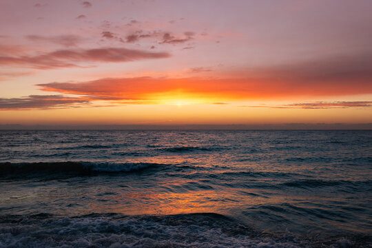 The magnificent colorful sunset sky with vibrant purple, pink, and orange hues reflected in the wet sand and gentle waves of the sea coast