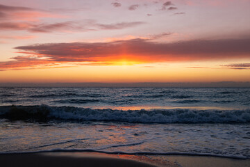 The magnificent colorful sunset sky with vibrant purple, pink, and orange hues reflected in the wet sand and gentle waves of the sea coast © castenoid