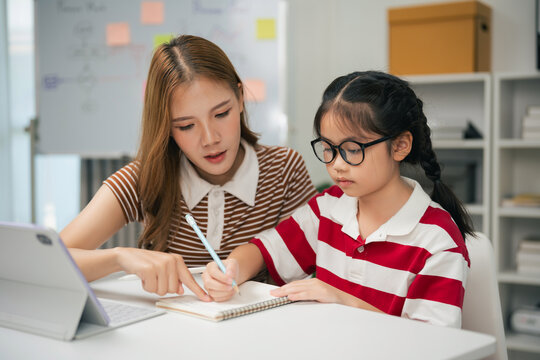 Young female tutor helping school-age girl with homework at desk in bright modern learning environment