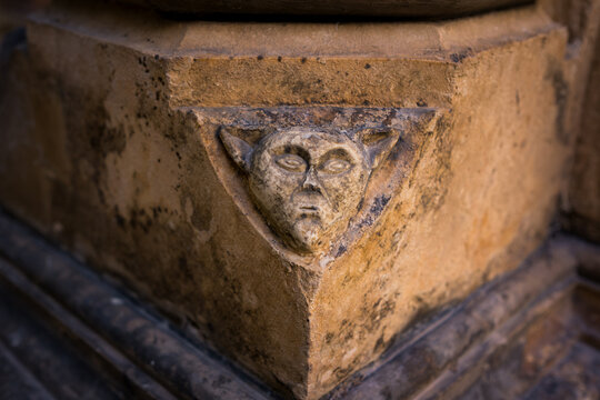 Close up of a weathered grotesque stone face with pointed ears carved into Gothic architecture at Batalha Monastery in Portugal