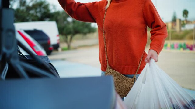Woman placing bags of fresh fruit into trunk of parked car after grocery shopping. Everyday errands, transporting food purchases, healthy lifestyle, convenient shopping, routine activities in parking