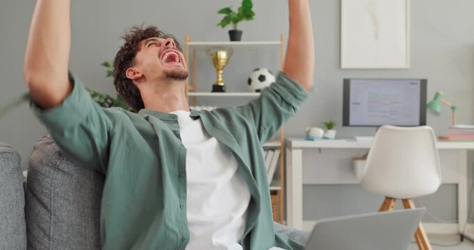 Young man uses laptop for online learning. Smiling student sits in bright home interior with computer for remote education and focused coursework. Modern e-learning supports flexible study.
