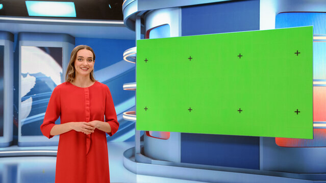Female News Anchor Presenter Standing Beside an Empty Green Screen Chroma Key Display With Tracking Markers and Speaking to the Camera While Delivering a News Segment in a Live Television Studio