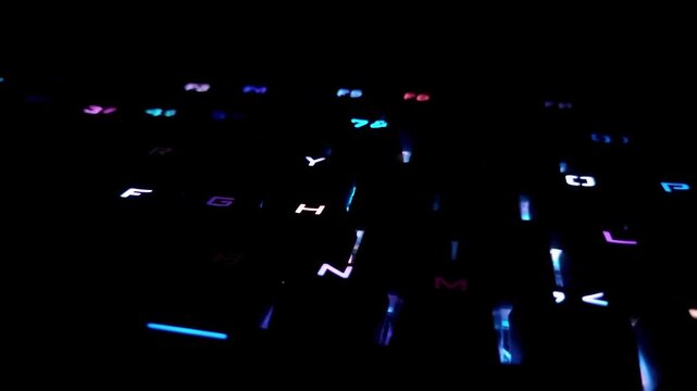 A close-up of a mechanical gaming keyboard in a dark room. The keyboard is equipped with a bright and dynamic RGB backlight.