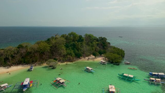 Aerial drone footage of CYC Beach in Coron, Palawan, Philippines, featuring traditional Filipino outrigger boats anchored in shallow turquoise waters beside a small white sand beach 