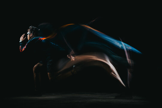 Action shot of male runner in starting pose with long exposure light trails and motion blur on dark background