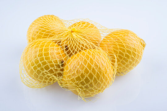 Lemons in yellow net bag on white studio background