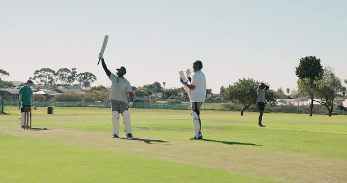 Male batsman is raising bat on suburban park pitch while wearing helmet near wicket stumps