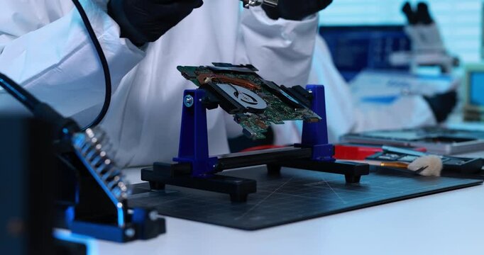 Technician in protective gloves repairs a circuit board with a soldering iron at an electronics workbench in a modern laboratory.