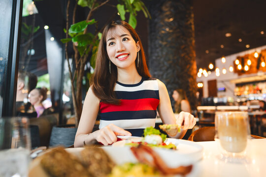 Beautiful smile asian woman healthy eating breakfast menu at restaurant sitting near window indoors on day