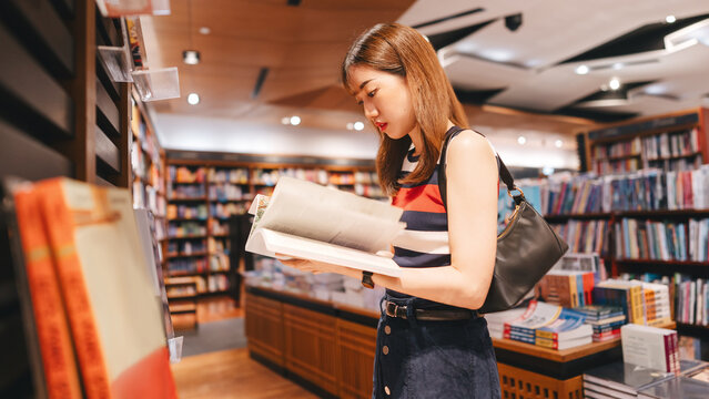 Adult asian woman reading book at bookstore shop choosing from bookshelf