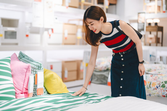 Adult asian woman choosing bed home interior shopping buying new furniture for bedroom at warehouse superstore