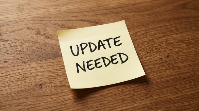 Yellow Sticky Note with 'Update Needed' on Wooden Desk
