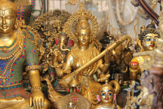 A golden brass statue of Goddess Saraswati playing the veena instrument at a shop window.