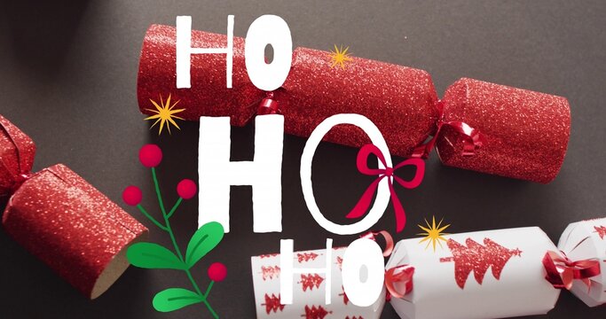 White HO lettering resting on surface with red glitter crackers and holly, copy space