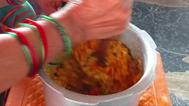 Person stirring cooked lentils inside an aluminum pot in a kitchen hands cooking dal preparation food
