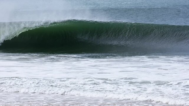 A long green wall peels into a clean open barrel, offshore spray streaming off the lip as it keeps spitting in slow motion at Supertubos beach.