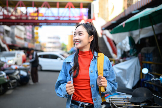 Happy Young Asian Woman Traveler Smiling in Chinatown Street with Yellow Backpack and Sunglasses
