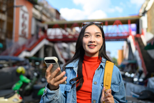 Smiling young Asian woman holding phone for navigation in a vibrant Chinatown district, ideal for travel, tourism, and technology concepts