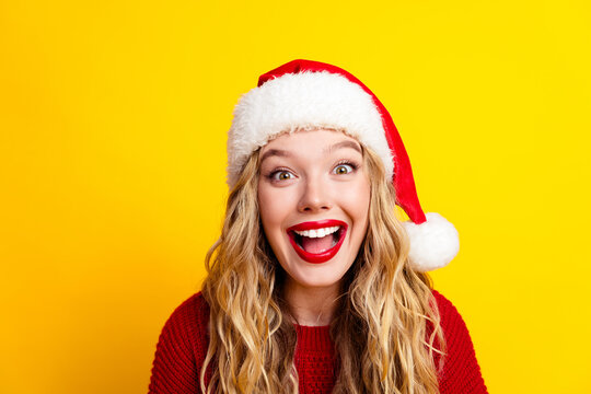 Happy young woman wearing a Santa hat and red sweater laughing on a bright yellow background celebrating Christmas joy and festive holiday spirit