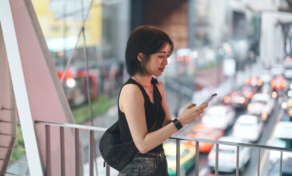 Asian woman walking in downtown with traffic jam using smartphone gps maps and calling taxi