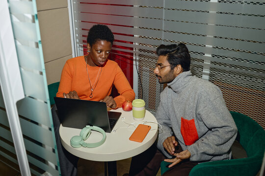 African American young adult woman and South Asian young adult man collaborating with laptop in office booth. Visualizing teamwork concept for corporate training website