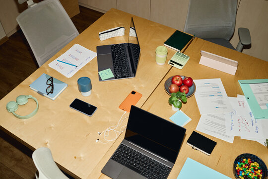 High angle view of meeting table with laptops, documents and stationery representing corporate teamwork. Suitable for business planning and workspace concept