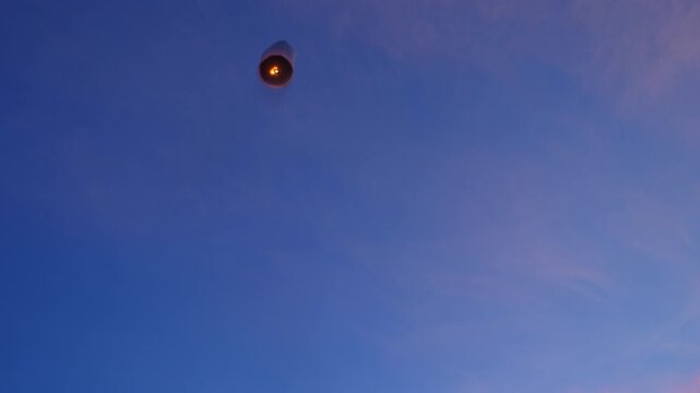 Woman releases a sky lantern into the twilight&mdash;a symbol of hope, celebration, and peace&mdash;during a traditional Asian festival, set against a beautiful sky.