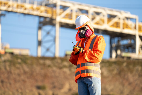 Industrial worker in safety gear checking a radio beside a large construction structure