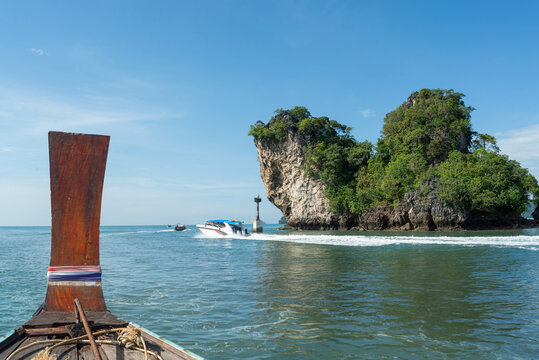 Traditional wooden longtail boat prow sailing past limestone island and speedboat in tropical turquoise sea